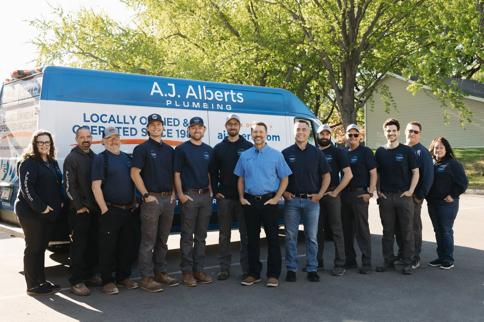 The AJ Alberts Plumbing and Water Conditioning team standing in front of their Woodbury showroom and service van